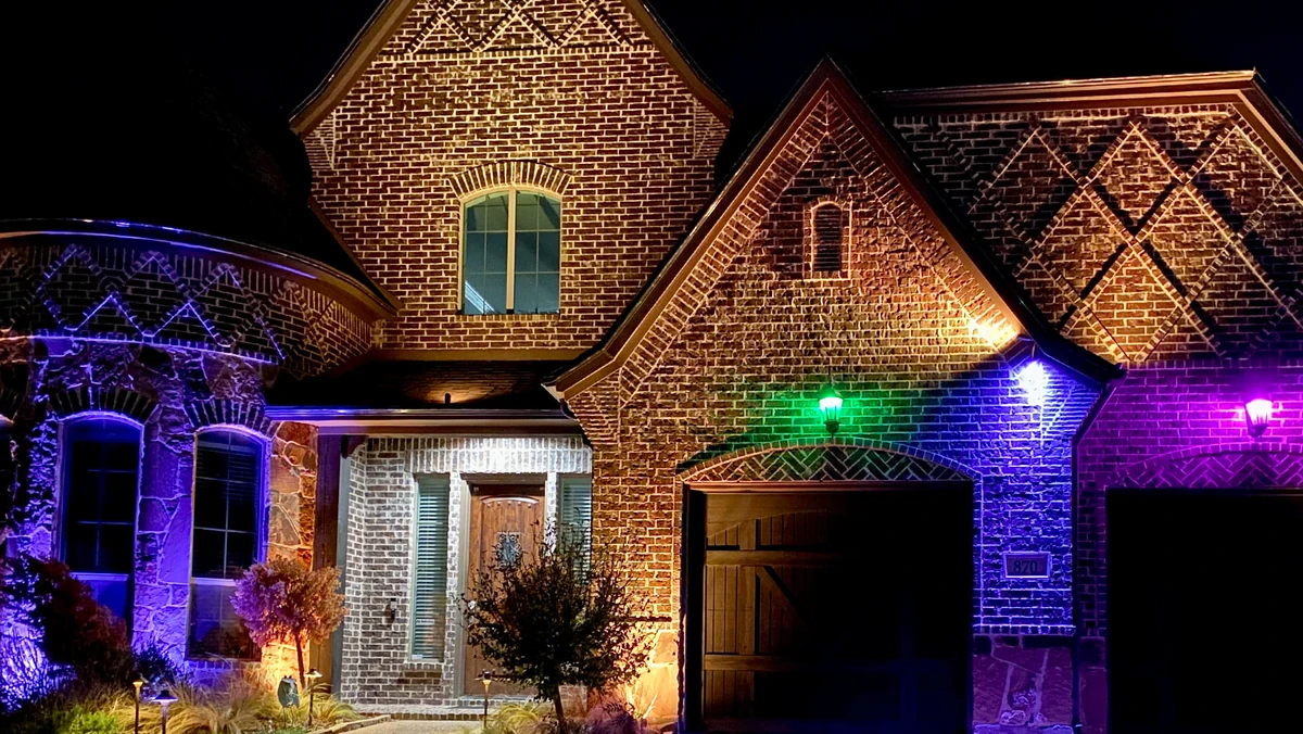 Multi-color permanent roofline lighting on a brick home at night by Optic Lighting
