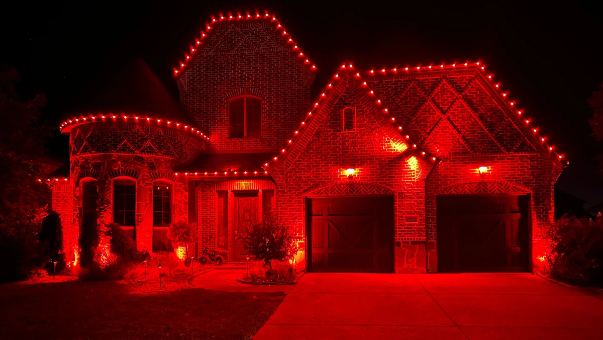 Red permanent roofline lighting on a brick home at night by Optic Lighting